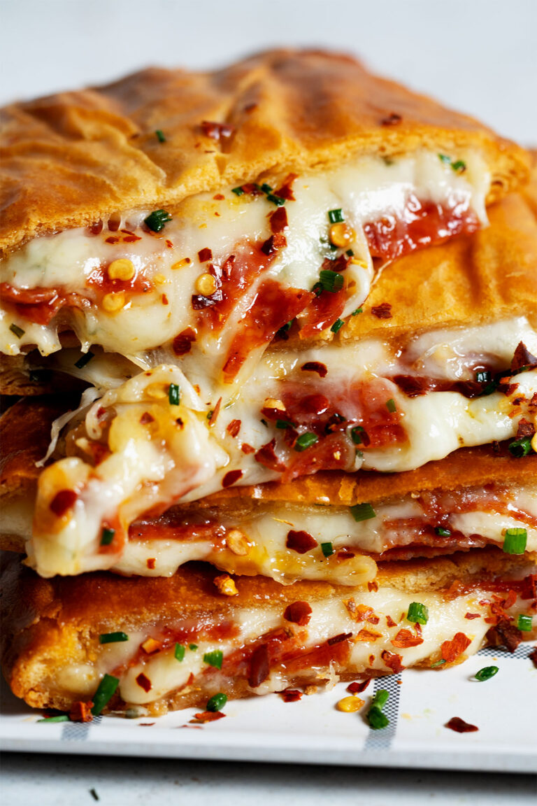 Golden brown pizza pockets stacked on a plate with dipping sauce