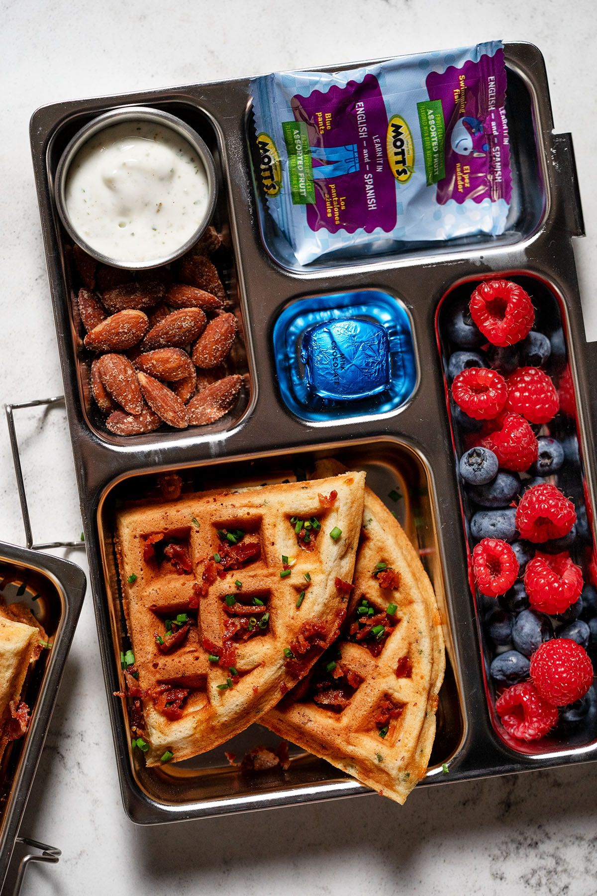Bento-style school lunch with savory waffles, ranch dip, seasoned almonds, fruit snacks, and mixed berries—kid-friendly and easy to pack.