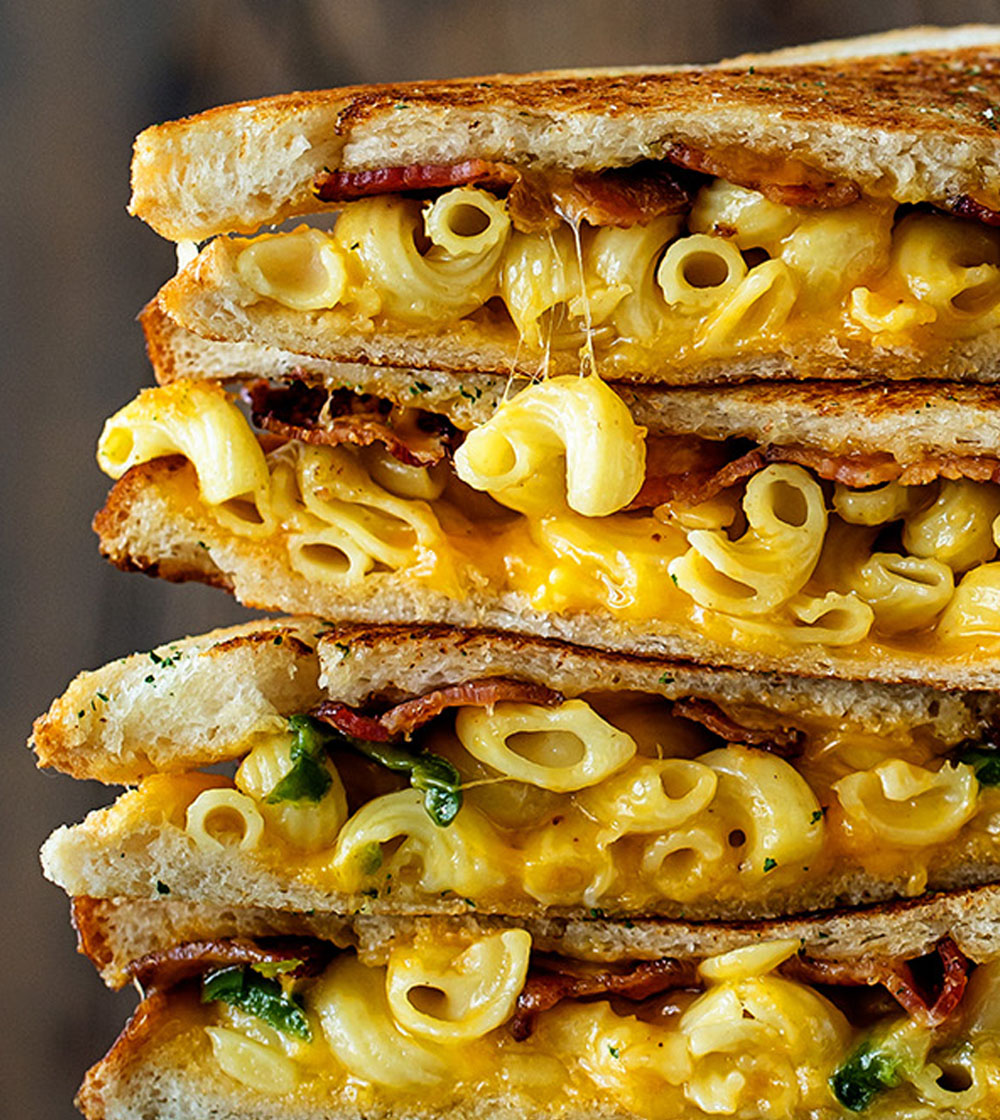 Grilled sandwich with mac and cheese and crispy bacon spilling out from golden toasted bread