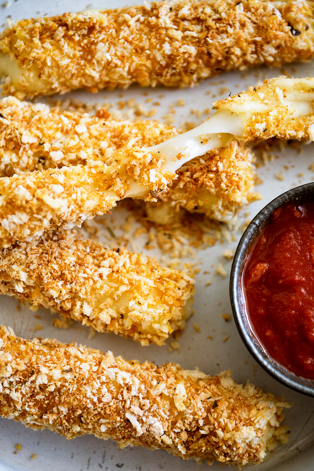 Plate of crispy baked mozzarella sticks with stretchy cheese and a side of marinara dipping sauce
