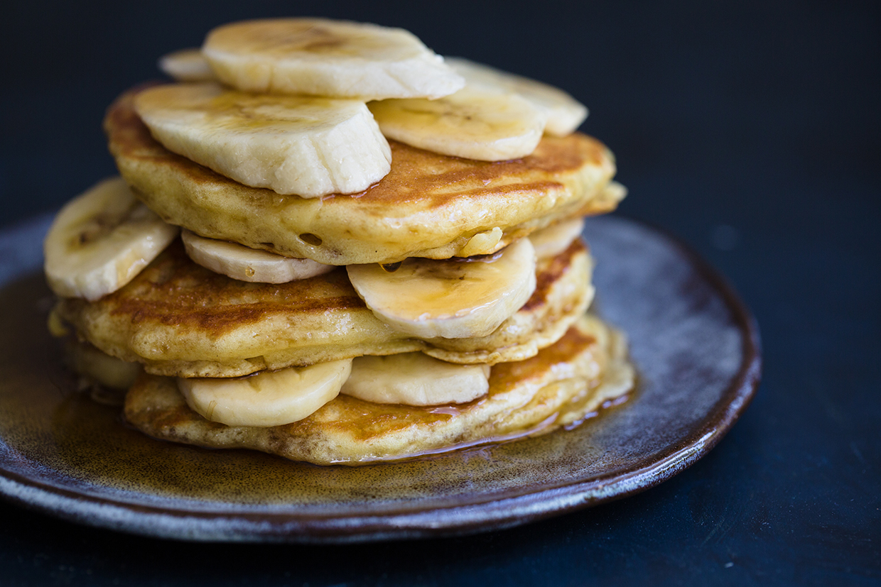 Stack of fluffy banana pancakes drizzled with honey and topped with banana slices on a white plate