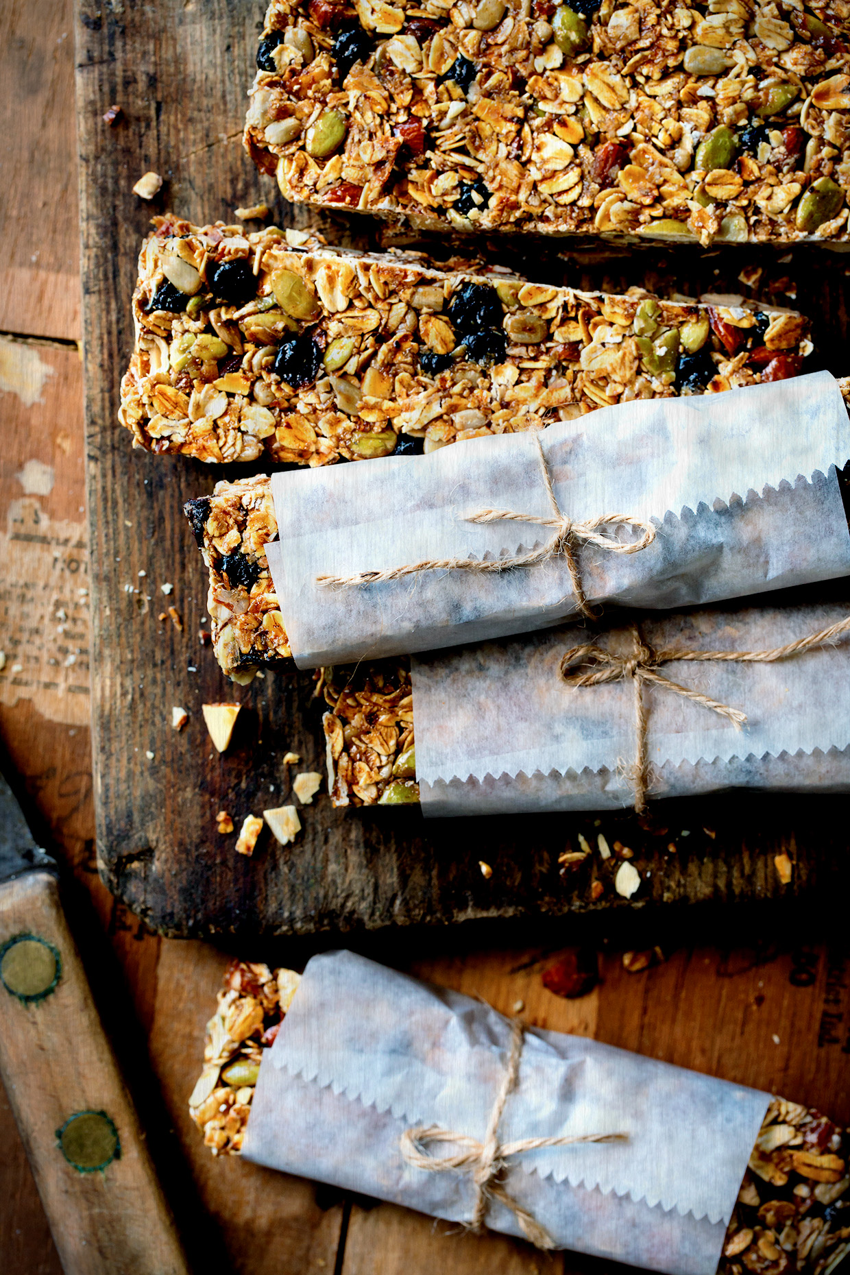 Chewy granola bars with visible oats and dried blueberries cut into squares and stacked on parchment paper