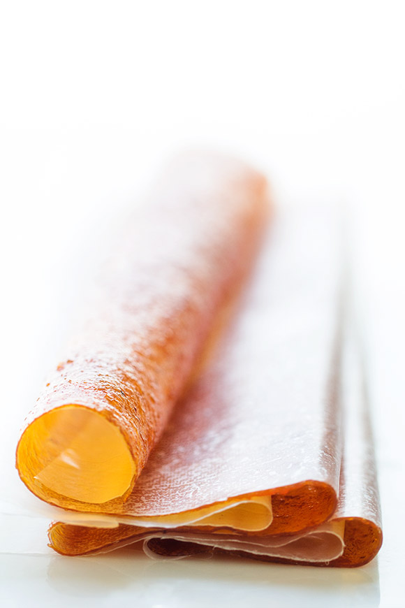 Homemade fruit roll-ups rolled into spirals with a glossy finish, shown on parchment paper