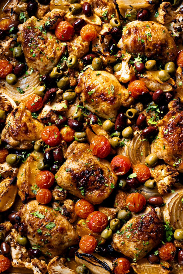 Sheet pan chicken tagine with cauliflower, red onion, and green olives, garnished with herbs