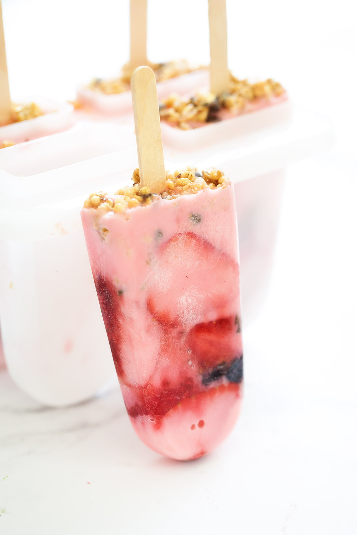 Layered strawberry yogurt popsicles with visible fruit swirls, stacked on a white surface with fresh strawberries nearby